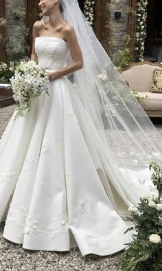 a woman in a white wedding dress standing next to a flowered arch with flowers on it