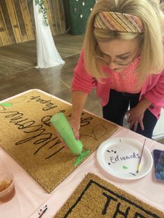 a woman is decorating a door mat with green paint and writing on the floor