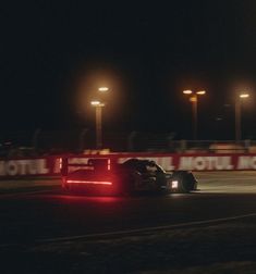 a race car driving down a track at night time with lights on the side of it