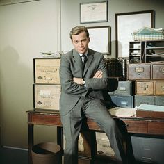 a man in a suit and tie sitting on a desk with many boxes behind him