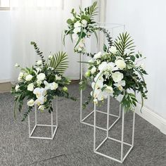 two vases with white flowers and greenery in them on carpeted room floor