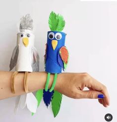 two paper birds sitting on top of each other in front of a hand with bracelets