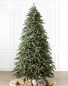 a christmas tree with lights and presents on the floor in front of a white wall