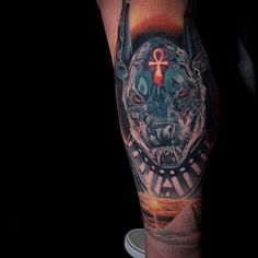 a man's leg with a tattoo on it that has a dog and an egyptian cross