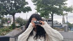 a woman holding up a camera in front of her face and covering her eyes with both hands