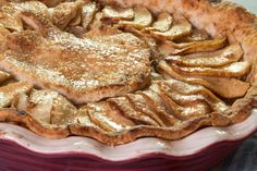 an apple pie with some powdered sugar on top in a red and white dish