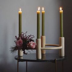 four candles are arranged on a table with flowers in the center and one candle is lit