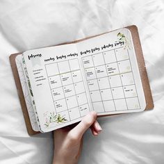 a person is holding a planner in their hand on a white sheet with flowers and leaves