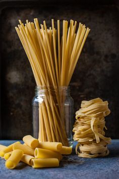 some pasta sticks are in a glass jar and next to it is a pile of noodles