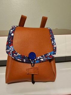 a brown leather backpack with blue and red flowers on the front, hanging from a hook