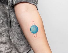 a woman's arm with a small blue planet tattoo on the left inner arm