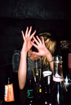 a woman sitting at a table with her hands in the air and two empty wine glasses