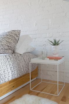 a bedroom with white brick walls and wood flooring, a bed with two pillows on it