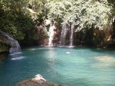 there is a waterfall in the middle of this pool with blue water and green trees