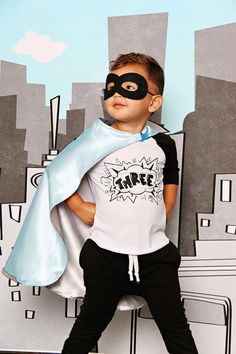 a young boy wearing a mask and cape standing in front of a cityscape