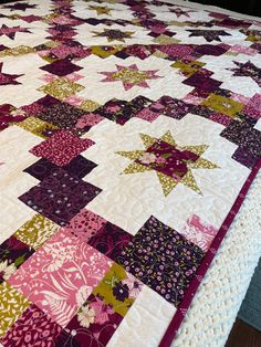 a large quilt is laying on top of a bed with purple and green colors in it