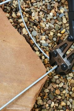 a pair of scissors is on the ground next to some rocks and gravel with a wire fence in the background