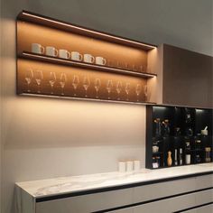 a white counter topped with lots of bottles and glasses next to a wall mounted shelf