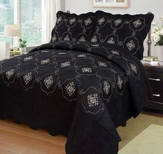 a black bedspread with white flowers on it in a room next to a window