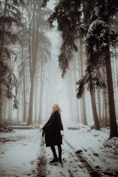 a woman standing in the middle of a snow covered forest