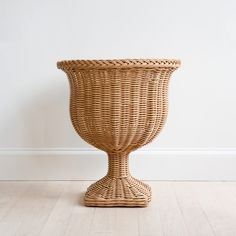 a wicker vase sitting on top of a wooden floor next to a white wall