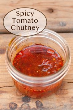 a jar filled with tomato sauce sitting on top of a wooden table next to a sign that says spicy tomato chutney