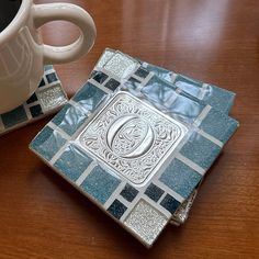 there is a coffee cup on the table next to a small square tile coasters