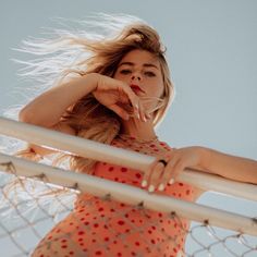 a woman in an orange dress leaning on a fence