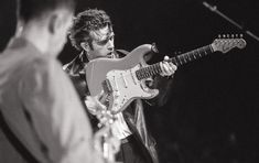 the man is playing an electric guitar on stage while another person stands nearby and looks at him