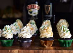 cupcakes with white frosting and green sprinkles next to a bottle of booze