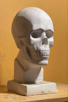 a white skull statue sitting on top of a wooden table next to a yellow wall