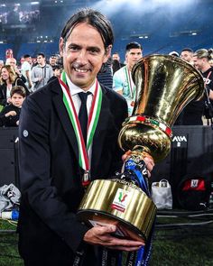 a man in a suit holding up a trophy and wearing a gold cup around his neck