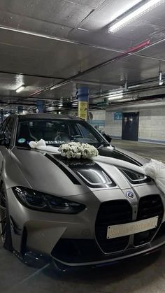 a silver sports car parked in a parking garage next to a white flower arrangement on the hood