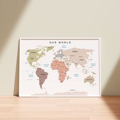 a framed map of the world on a wooden table in front of a beige wall