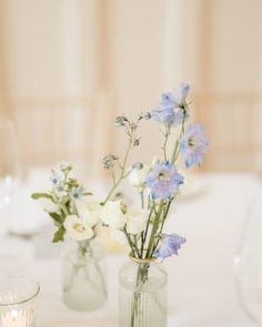 two vases filled with flowers on top of a table next to a glass candle