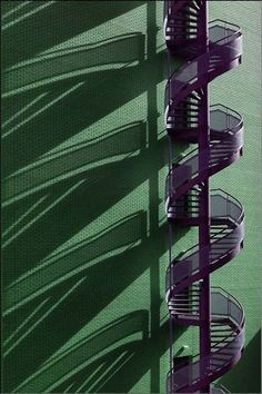 a spiral staircase in front of a green wall with shadows on the walls and floor