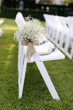 an outdoor ceremony with white chairs and baby's breath flowers on the back of them