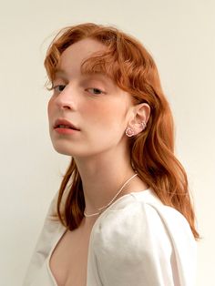 a woman with red hair wearing a white shirt and pearl necklace, looking off to the side