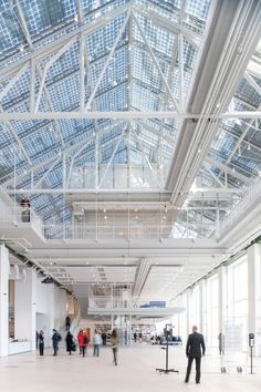 people are walking around in an empty building with many windows and metal beams on the ceiling