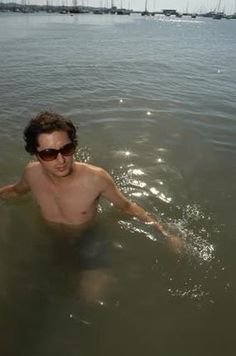 a shirtless man in the water with sunglasses on his head and one eye open