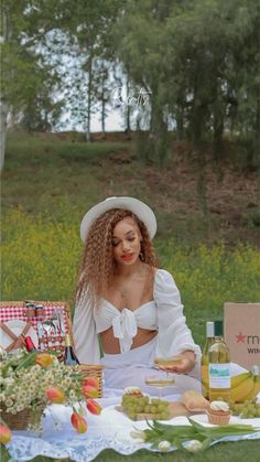 a woman sitting on the grass with food and wine in front of her at an outdoor picnic