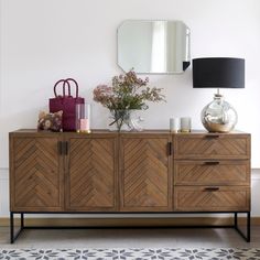 a wooden dresser sitting next to a mirror and vase on top of it's sideboard