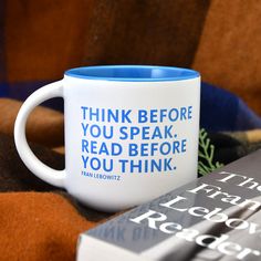 a blue and white coffee mug sitting on top of a blanket next to a book