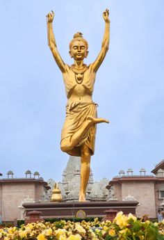 there is a large golden statue in front of the building with many flowers around it