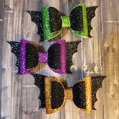 three different colored bows with black and gold glitters on them sitting on a wooden surface