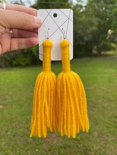 a pair of yellow tasselled earrings hanging from a string in front of a field