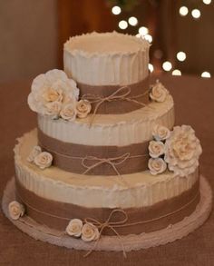 three tiered wedding cake with white flowers and burlocks on the bottom layer