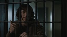 a man in a jail cell with his hand on the bars and looking at something