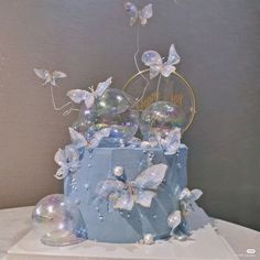 a blue cake with butterflies on it and bubbles in the shape of flowers, sitting on a table