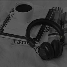 black and white photograph of headphones, notebooks, and cup of coffee on a bed